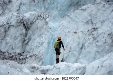 Equiped Man In Shorts Standing In Front Of A Waterfall In An Ice Wall In A Glacier. Iceland