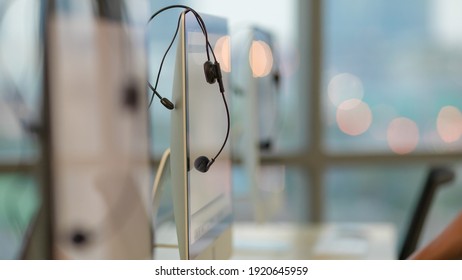 Equipment of call center, eadphone headset hang on computer screen in office in thte evening with blur bokeh of light in background. - Shutterstock ID 1920645959