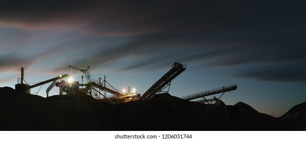 Equipment for crushing rock and sorting into fractions at a mining enterprise. Silhouettes of constructions against the background of evening sky, panorama.