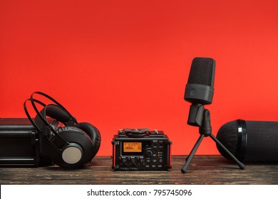 equipment for field audio recording on red background. usb microphone, recorder, headphones, portable case and windshield