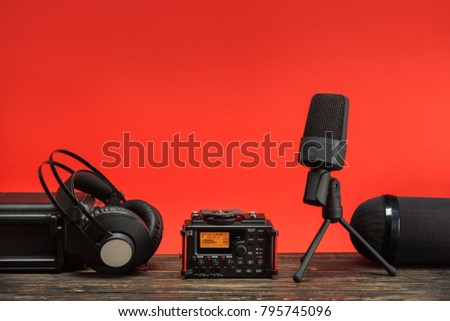 equipment for field audio recording on red background. usb microphone, recorder, headphones, portable case and windshield