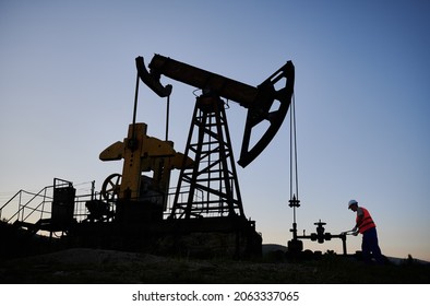 Equipment For Oil Industry. Power Engineer With Wrench Regulating Operation Of The Pipeline. Drilling Rig For Fossil Fuel Extraction. Pump Rocker-machine On The Background Of Cloudless Blue Sky.