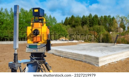 Equipment for surveyor. Optical theodolite near foundation. Surveyor device. Construction site with foundation. Equipment for surveyor on tripod. Construction house in countryside. Geodesy topography