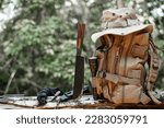 Equipment for survival bucket hat backpack hiking knife camping flashlight resting on wooden timber in the background is a forest