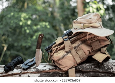 Equipment for survival bucket hat backpack hiking knife camping flashlight resting on wooden timber in the background is a jungle - Powered by Shutterstock