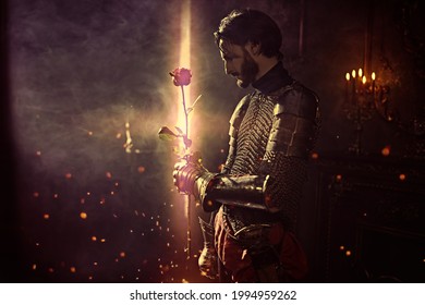 The era of romanticism. Portrait of a noble knight in armor with a red rose in his hands standing in a castle.