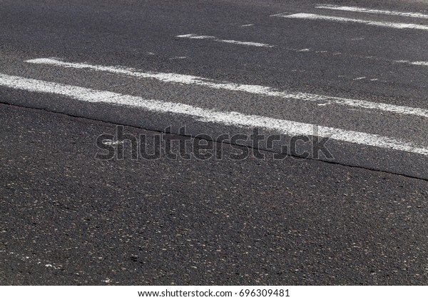 Erased road markings at\
the crossing point through the pedestrians. Photo close-up of a\
black asphalt road
