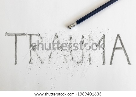 Erasing trauma. Trauma written on white paper with a pencil, partially erased with an eraser. Symbolic for overcoming trauma or treating trauma.  