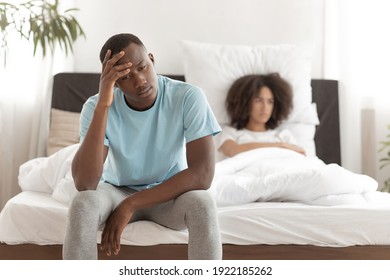 Erectile dysfunction, male power, quarrel, sex problems and relationship. Sad frustrated young african american guy sits on bed, offended female looks to side in bright interior of bedroom, free space