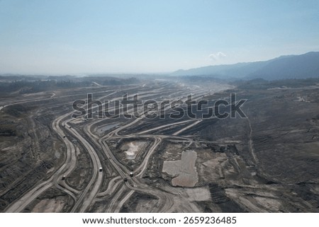 erial view of a large open pit mine with visible terraced layers of earth. A substantial body of water, likely an accumulation of runoff, occupies the bottom of the pit.