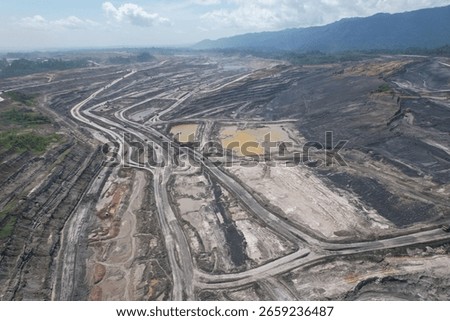 erial view of a large open pit mine with visible terraced layers of earth. A substantial body of water, likely an accumulation of runoff, occupies the bottom of the pit.