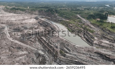 erial view of a large open pit mine with visible terraced layers of earth. A substantial body of water, likely an accumulation of runoff, occupies the bottom of the pit.
