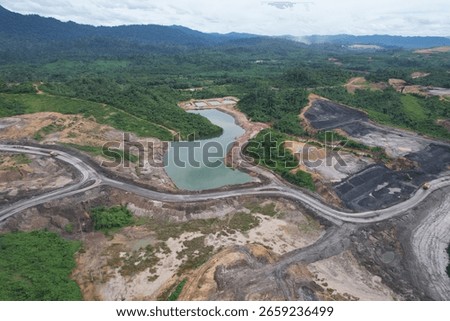 erial view of a large open pit mine with visible terraced layers of earth. A substantial body of water, likely an accumulation of runoff, occupies the bottom of the pit.