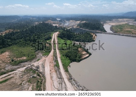 erial view of a large open pit mine with visible terraced layers of earth. A substantial body of water, likely an accumulation of runoff, occupies the bottom of the pit.