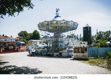 ERLANG, GERMANY - Jun 11, 2019: A Light Blue Merry Go Round With Tropical Birds And A Fairy Sitting On Top Surrounded By A Couple Of People