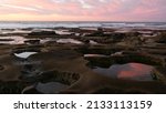 Eroded rock formation, tide pool shape in La Jolla, California coast, USA. Littoral intertidal zone erosion, tidepool relief. Sunset sky reflection in water, cavity, hollows and holes on stone surface