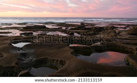 Eroded rock formation, tide pool shape in La Jolla, California coast, USA. Littoral intertidal zone erosion, tidepool relief. Sunset sky reflection in water, cavity, hollows and holes on stone surface