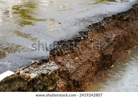 The erosion and reshaping of asphalt along the edge of a residential water channel
