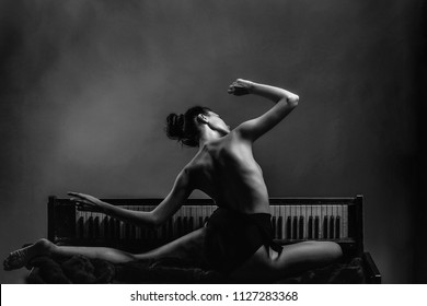 Erotic music. young girl or woman dancer with sexy flexible body of ballerina and naked back posing on old retro wooden piano on grey background