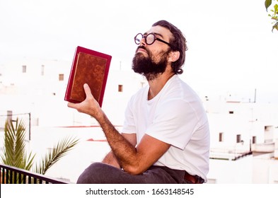 erudite young person with a beard and glasses with his lost gaze holding some books