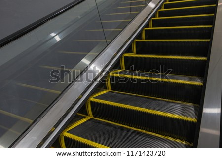 Escalator in the basement. Step up the escalator staircase. Yellow bars, steel bars, yellow iron bars
