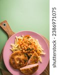 Jägerschnitzel escalope chasseur a East German DDR GDR specialty of breaded fried sausage slice, tomato sauce, Macaroni Penne pasta, parsley on pink rose plate, cutlery, wooden board, green background