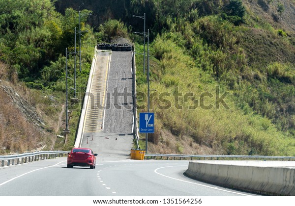 Escape Lane ahead uphill road signs on\
dual carriageway highway through mountains in scenic countryside.\
Red sedan coupe sports car driving on left hand side on two\
lane/double lane\
street/roadway.