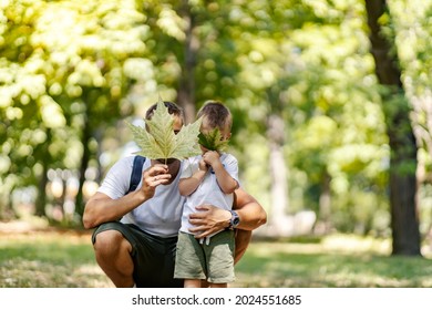 Escape To Nature And An Active Weekend. Holidays In The Woods, Family Fun In The Park. Father And Son Are Dressed In The Same Clothes Fooling Around With Leaves Dad Squats Next To The Boy And Hugs Him