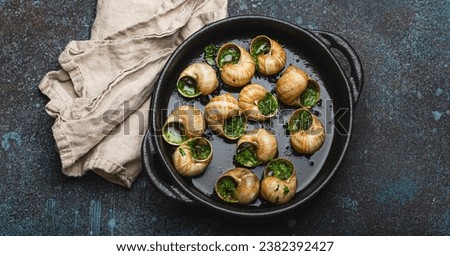 Escargots de Bourgogne Cooked Snails with Garlic Butter and Parsley in black cast iron pan on rustic stone background from above, traditional French Delicacy .