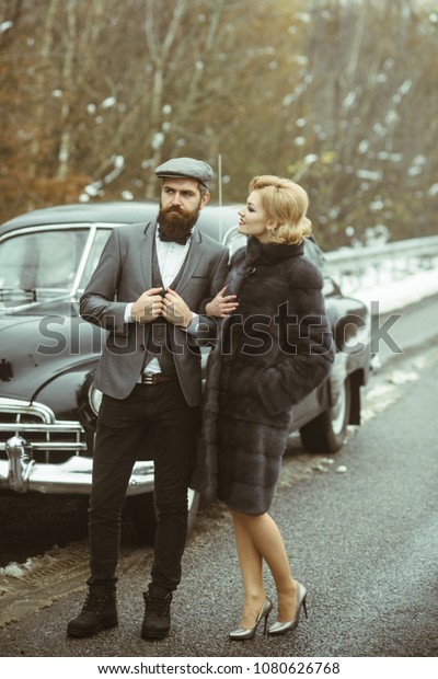 Escort of girl by security. Couple in love on\
romantic date. Bearded man and sexy woman in fur coat. Travel and\
business trip or hitch hiking. Retro collection car and auto repair\
by mechanic driver