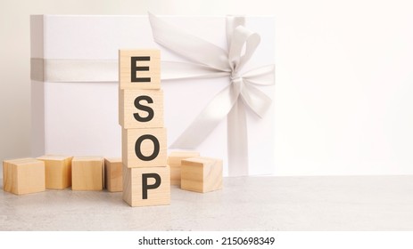 the ESOP text is laid out in a pyramid of wooden cubes. in the background is a paper gift box with a shiny white ribbon. ESOP - short for Employee Stock Ownership Plan