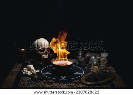 Esoteric mystical still life with a  burning altar bowl, pentagram, books, skull, potions and bones. Black magic ritual items on old wooden table.