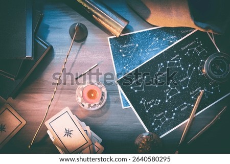 Esoteric study and prediction background detail with map with constellations, divination cards and retro objects on wooden table with books and magical atmosphere. Top view.