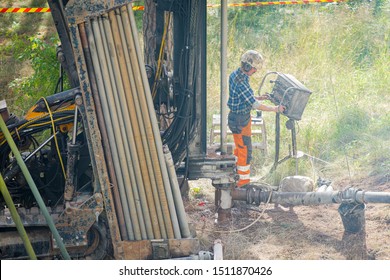 Espoo, FINLAND - JULY 3, 2019: Geothermal Heat Pump Installation In Eco Friendly Apartment House. Drilling Rig In Yard. Worker In Hard Hat Drilling A Borehole For Geothermal Heating System.  