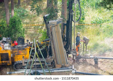 Espoo, FINLAND - JULY 3, 2019: Geothermal Heat Pump Installation In Eco Friendly Apartment House. Drilling Rig In Yard. Worker In Hard Hat Drilling A Borehole For Geothermal Heating System.  