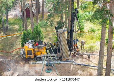 Espoo, FINLAND - JULY 3, 2019: Geothermal Heat Pump Installation In Eco Friendly Apartment House. Drilling Rig In Yard. Worker In Hard Hat Drilling A Borehole For Geothermal Heating System.  