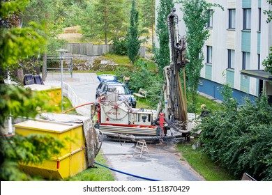 Espoo, FINLAND - JULY 5, 2019: Geothermal Heat Pump Installation In Eco Friendly Apartment House. Drilling Rig In Yard. Worker In Hard Hat Drilling A Borehole For Geothermal Heating System.  