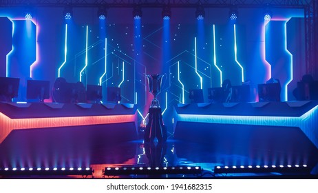 ESports Winner Trophy Standing On A Stage In The Middle Of The Computer Video Games Championship Arena. Two Rows Of PC For Competing Teams. Stylish Neon Lights With Cool Design.