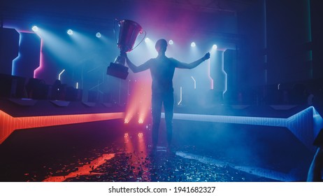 eSports Winner Trophy Standing on a Stage in the Middle of the Computer Video Games Championship Arena. Two Rows of PC for Competing Teams. Stylish Neon Lights with Cool Area Design. - Shutterstock ID 1941682327