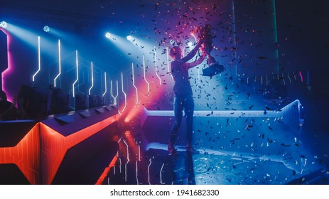 eSports Winner Trophy Standing on a Stage in the Middle of the Computer Video Games Championship Arena. Two Rows of PC for Competing Teams. Stylish Neon Lights with Cool Area Design. - Shutterstock ID 1941682330