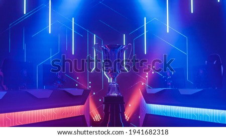 eSports Winner Trophy Standing on a Stage in the Middle of the Computer Video Games Championship Arena. Two Rows of PC for Competing Teams. Stylish Neon Lights with Cool Design.