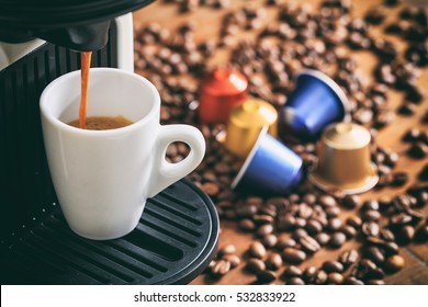 Espresso coffee capsules and machine maker on a wooden table, blur coffee pods and beans background