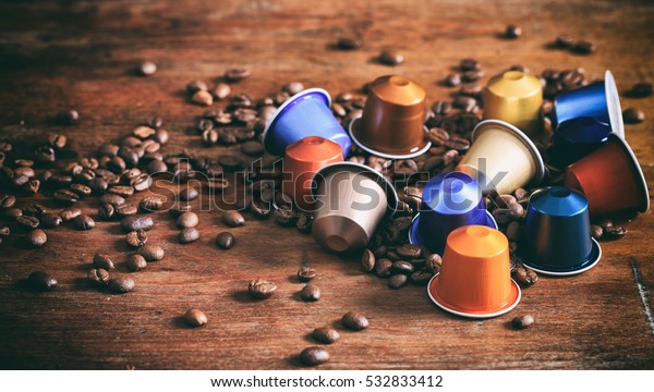 Espresso coffee capsules, pods and coffee\
beans on wooden\
background