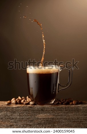 Espresso coffee glass cup with splashes on a brown background. Coffee cup and roasted coffee beans on a old wooden board.