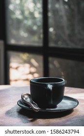 An espresso coffee shot in a black coffee mug on a table beside a glass window.