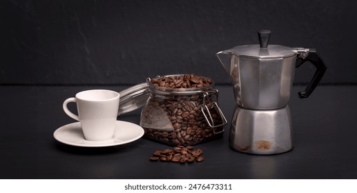 Espresso cup, moka pot and a jar of coffee beans on a black slate surface. Coffee concept.