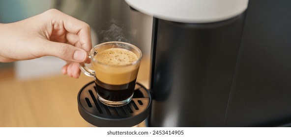 Espresso cup with steam and froth during Coffee making Coffee by Coffee Maker Machine on wood table bar. Cafe shop, Daily beverage drink at Home, Apartment and Office concept