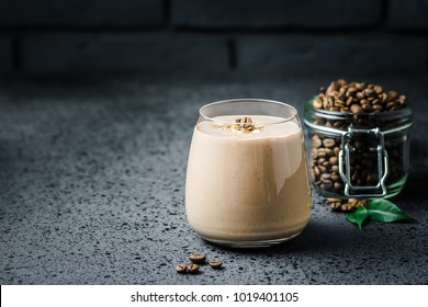 Espresso maca banana smoothie and coffee beans in glass jar on dark concrete background. Selective focus, space for text.