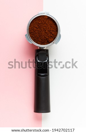 Espresso machine filte holder with ground coffee on pink and white background.