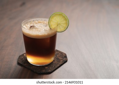 Espresso tonic in simple glass on walnut wood table with copy space , shallow focus